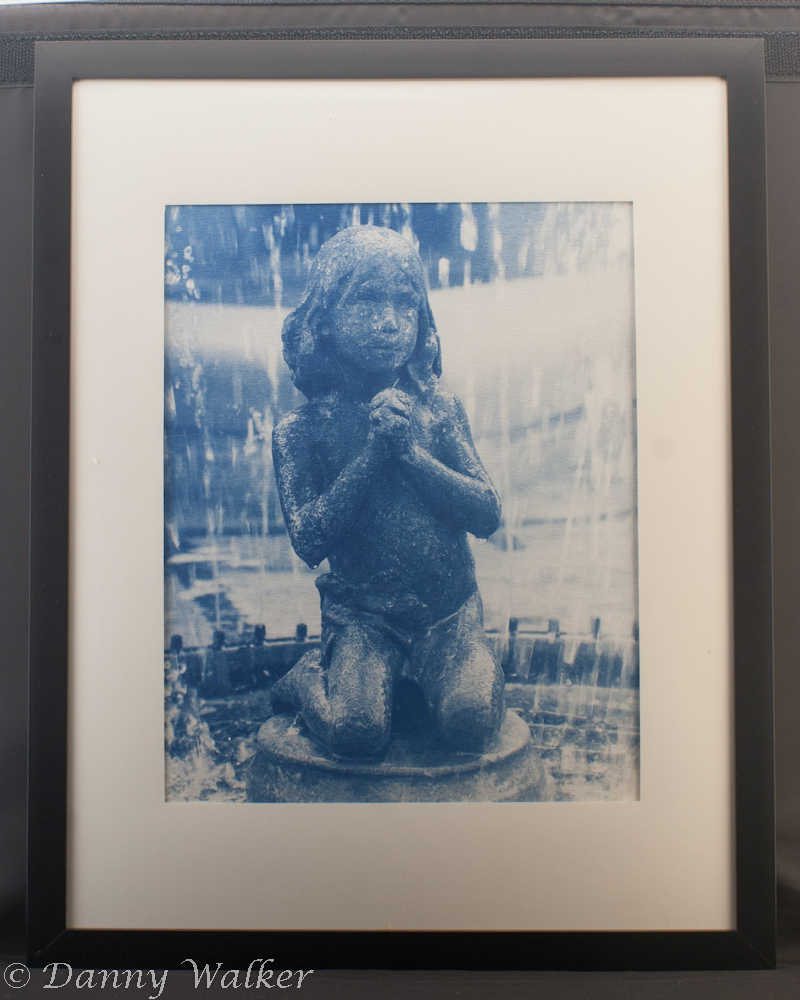 A cyanotype print of a statue of a praying child in a fountain.